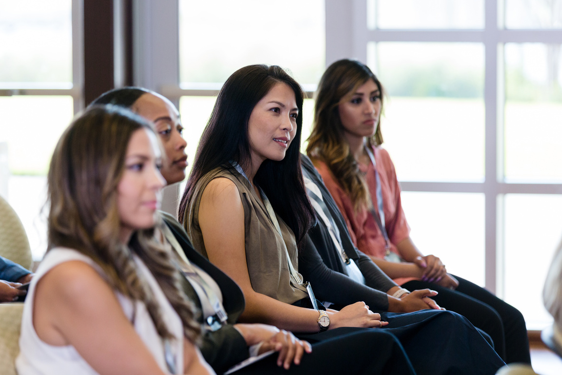 Diverse business women listen to unseen speaker at conference